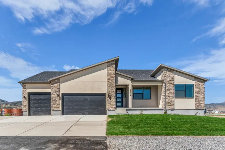 Contemporary stucco and stone exterior with a covered porch, dual garage doors, and a manicured lawn