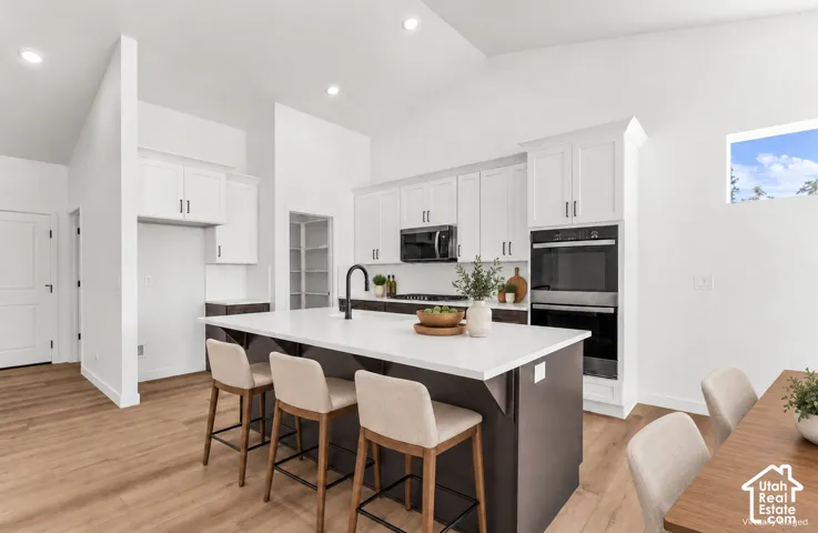 Kitchen featuring an expansive island with seating, dark lower cabinetry, white upper cabinetry, and a pantry with built-in shelving