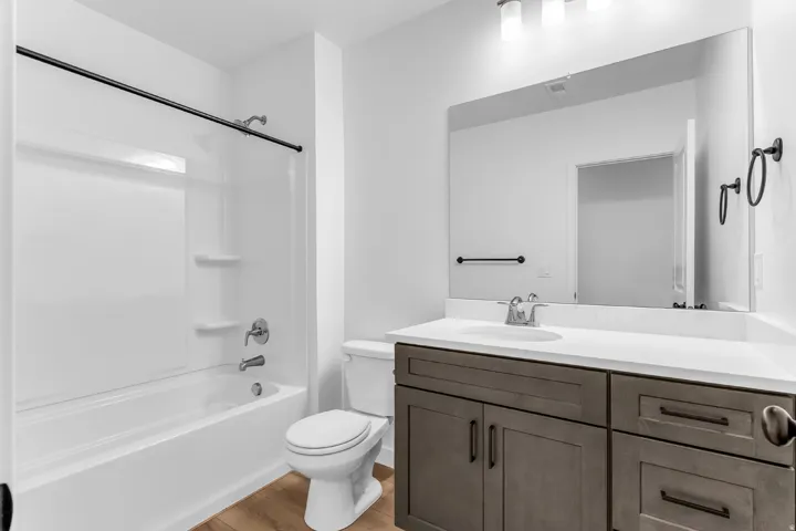 Bathroom featuring a white tub/shower combination, dark wood-finish vanity with a white countertop, and light wood-finish flooring