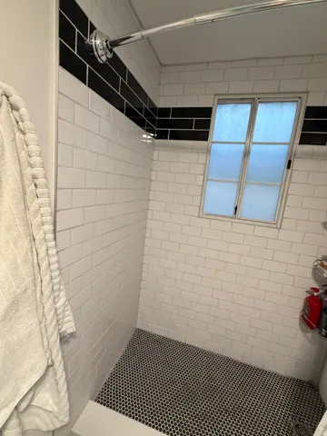 Subway tile shower surround with a black accent band, black penny tile flooring, and a frosted window