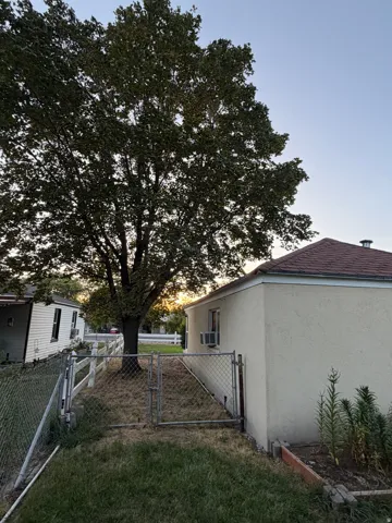 Exterior featuring a stucco finish, a shingled roof, a mature tree, a chain-link fence, and a raised garden bed