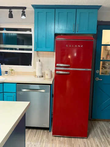 White tile backsplash, stainless steel dishwasher, wood-finish flooring, and a red retro-style refrigerator