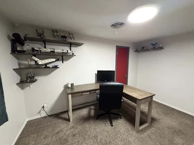 White walls with built-in shelving, gray carpet, and a red interior door