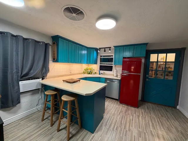 Kitchen featuring teal cabinetry, white countertops, tile backsplash, stainless steel dishwasher, and wood-finish flooring