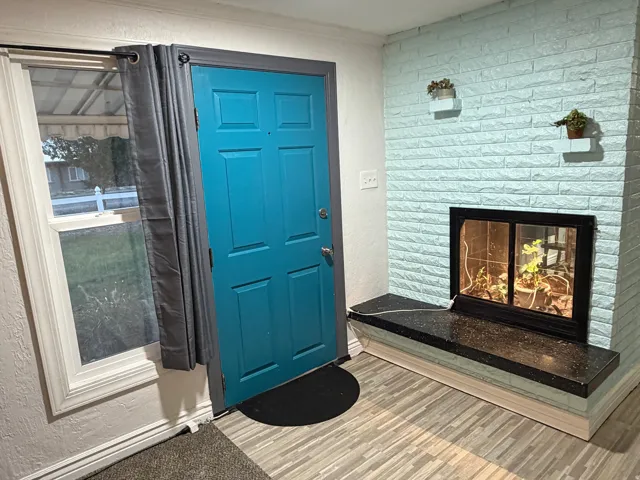 Entryway featuring a vibrant blue door, a window with white trim, a fireplace with a light blue brick surround, a black hearth, and wood-finish flooring