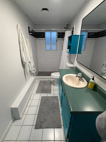 Tile flooring, vanity with integrated sink, wall-mounted mirror, subway tile shower surround, and window in shower