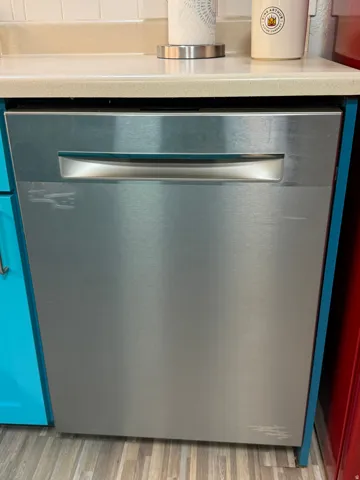 Stainless steel dishwasher with a bar handle, integrated into cabinetry, set beneath a neutral-toned countertop and wood-finish flooring