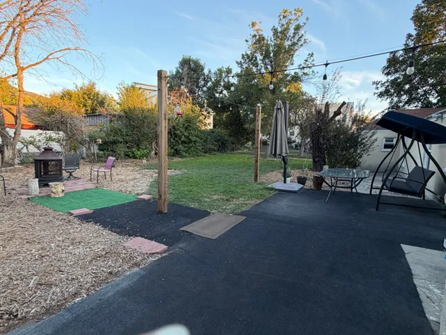 Expansive backyard featuring a large paved patio, manicured lawn, and mature trees