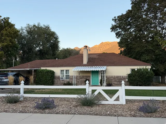 Single-story residence featuring a brown shingle roof, brick and stucco exterior, a turquoise entry door with a white metal awning, an attached carport, and a white picket fence