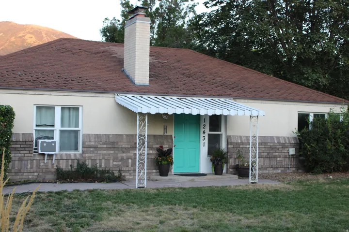 Front exterior featuring a vibrant turquoise entry door, a white metal awning with decorative supports, and a brick and stucco facade