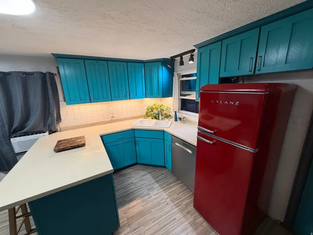 U-shaped kitchen featuring teal cabinetry, a white rectangular sink, light-toned countertops, white subway tile backsplash, and light wood-finish flooring
