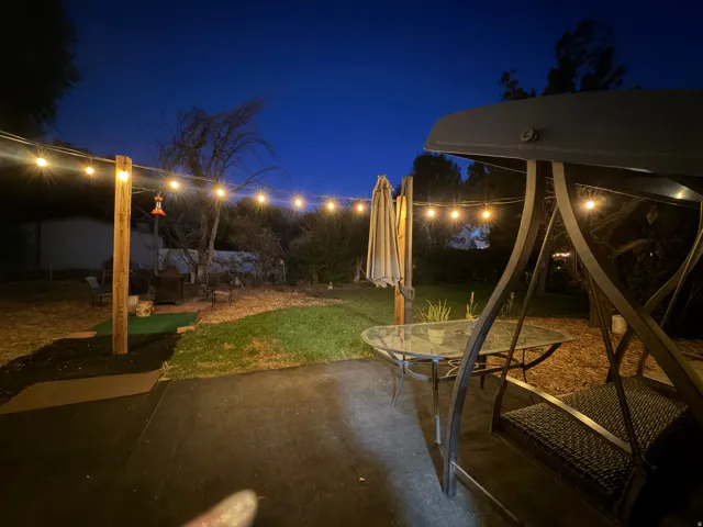 Paved patio area, string lighting, established trees, and a dedicated fire pit area