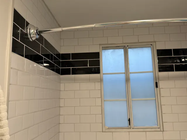 Subway tile shower surround with black accent band, featuring a frosted glass window
