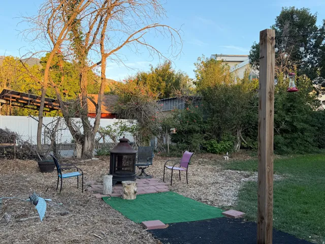 Woodchip ground cover, paved patio area, integrated fire pit, and mature trees