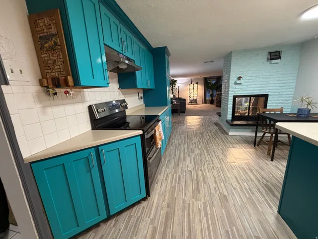 Kitchen featuring teal cabinetry, white subway tile backsplash, stainless steel electric range, and light-toned wood-finish flooring
