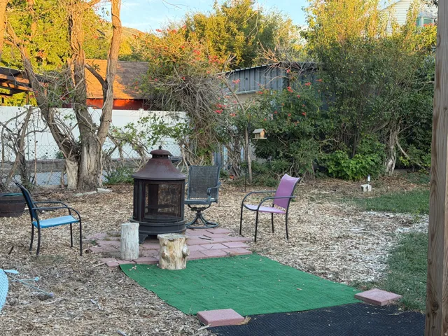 Outdoor area featuring a built-in fire pit on a brick paver base, surrounded by mature trees, and a perimeter fence