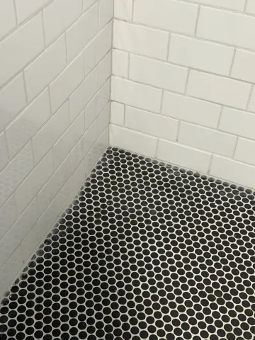 White subway tile walls with black penny tile flooring