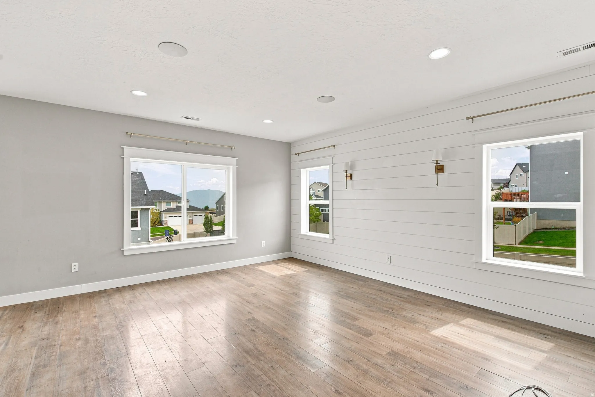 Wood-finish flooring with a shiplap accent wall, multiple windows, recessed lighting, and wall-mounted sconces