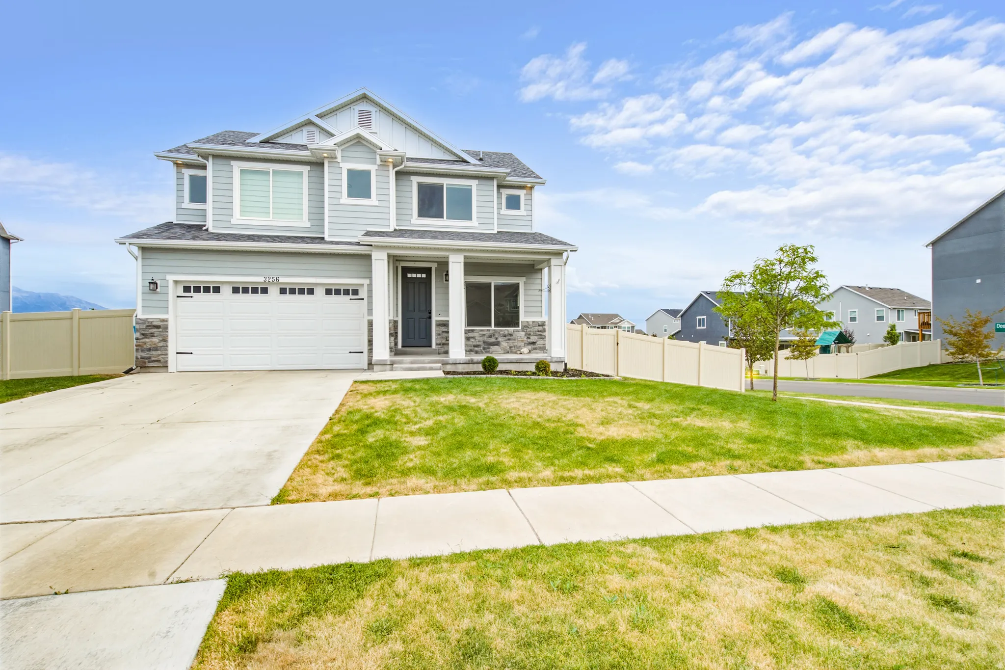 Light gray siding exterior, stone veneer accents, white trim, attached two-car garage, and concrete driveway