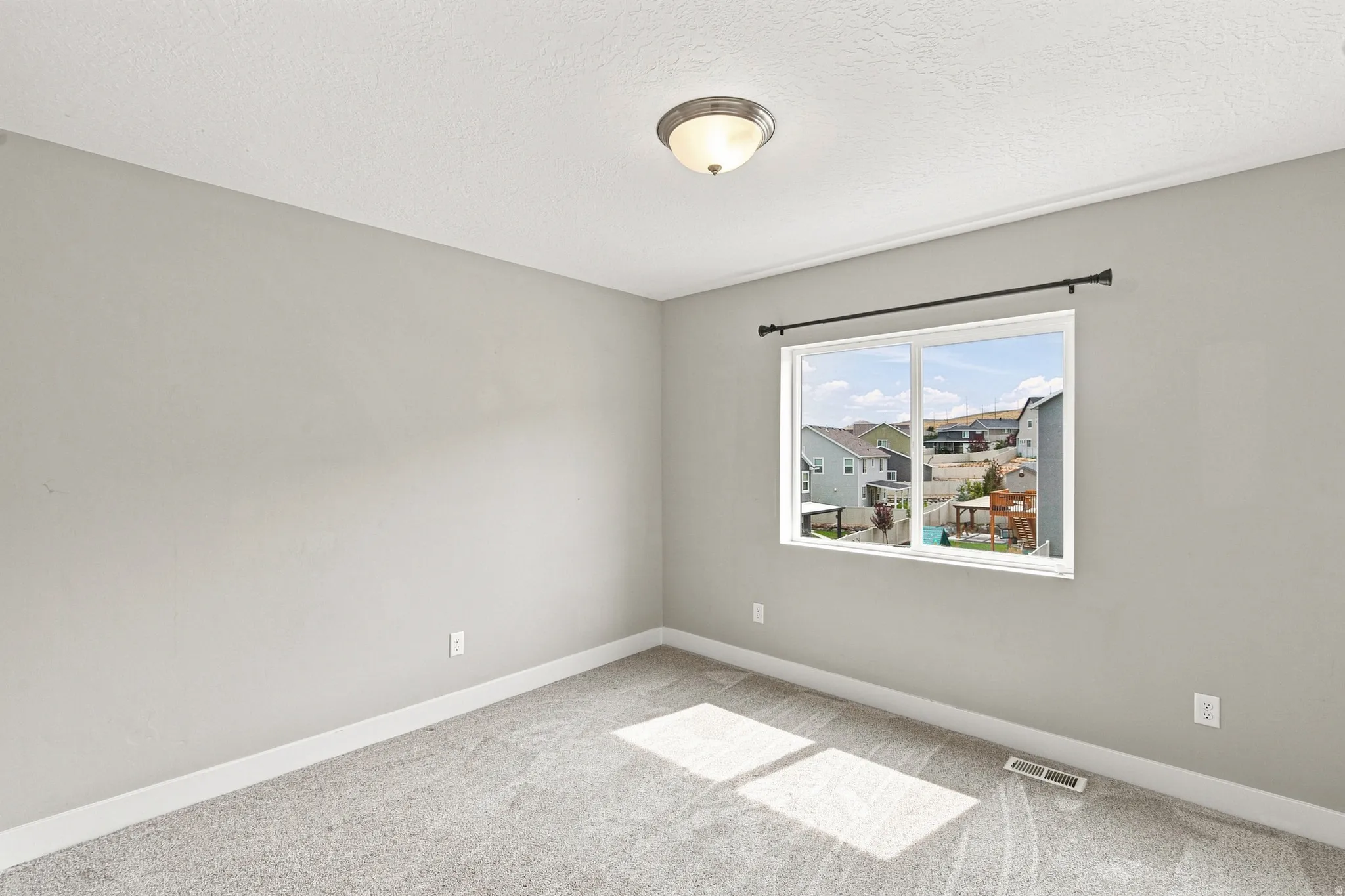 Recessed ceiling light fixture, neutral wall paint, carpeted flooring, and a large window with neighborhood views