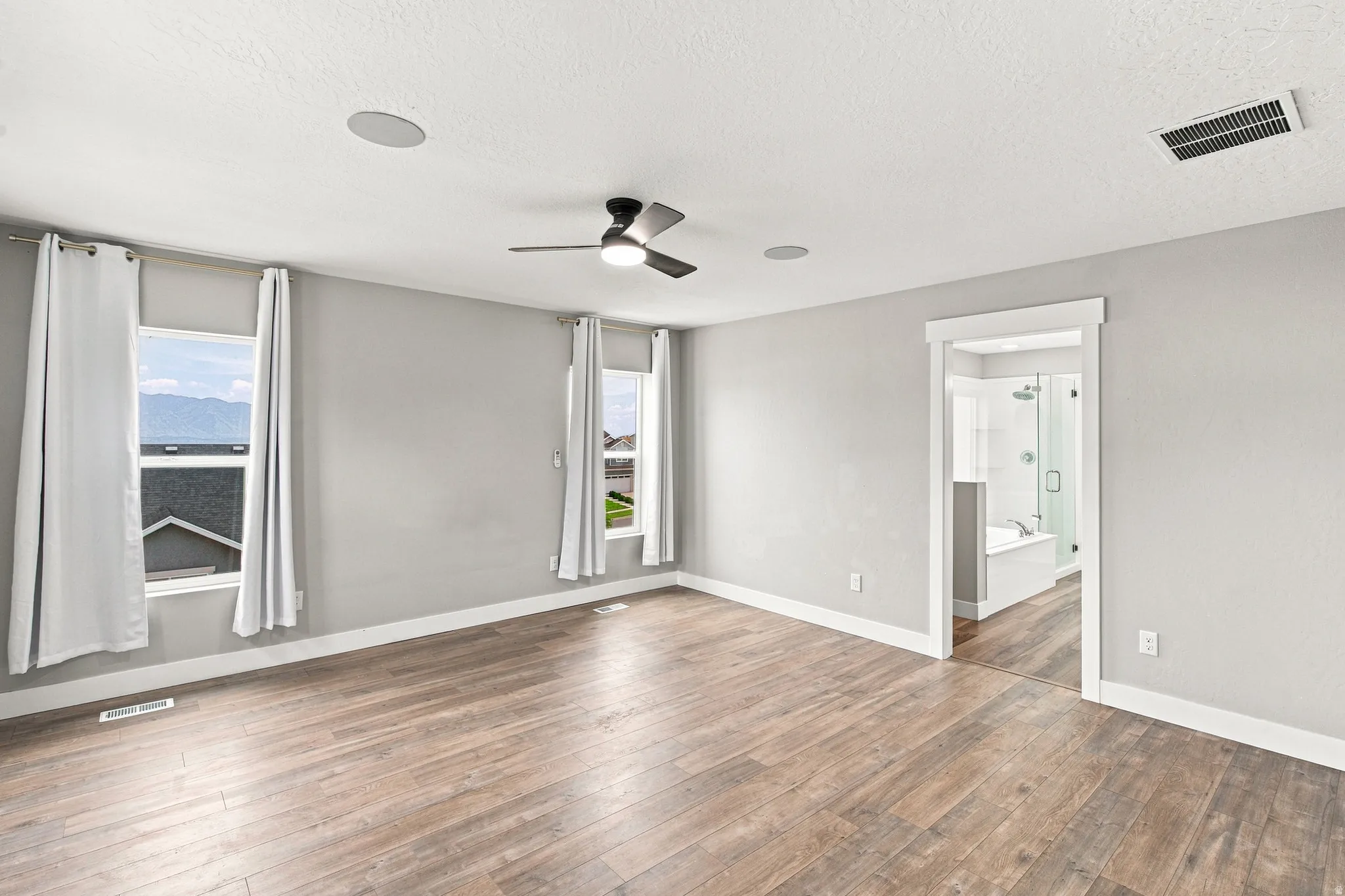 Wood-finish flooring, recessed ceiling speakers, ceiling fan, and an en-suite bathroom entrance with a shower and soaking tub