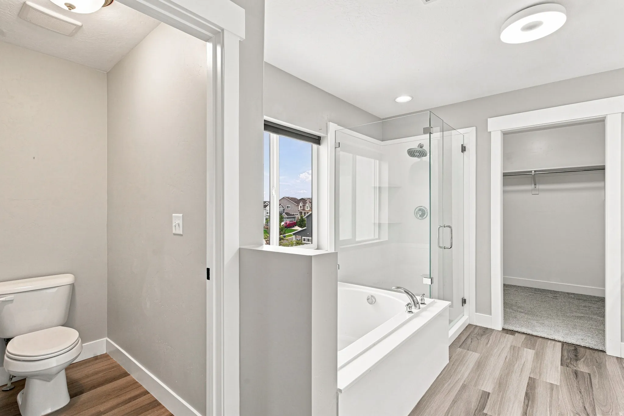 Walk-in shower with clear glass enclosure, built-in bathtub, wood-finish flooring, and a window for natural light