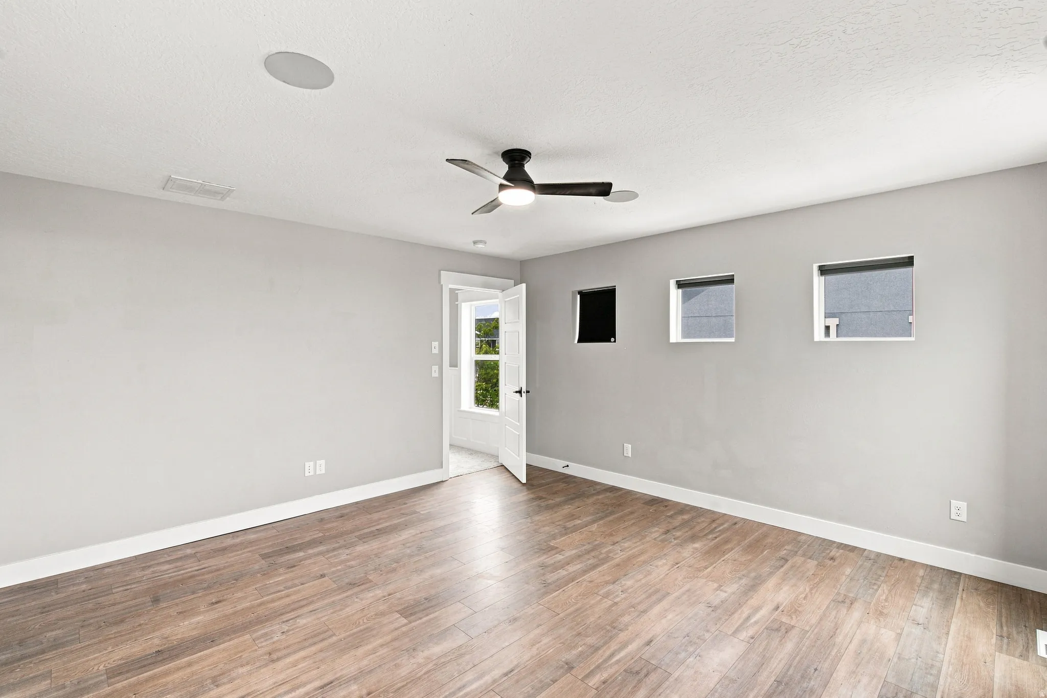 Recessed ceiling speaker, contemporary ceiling fan, three square windows, wood-finish flooring, white trim details