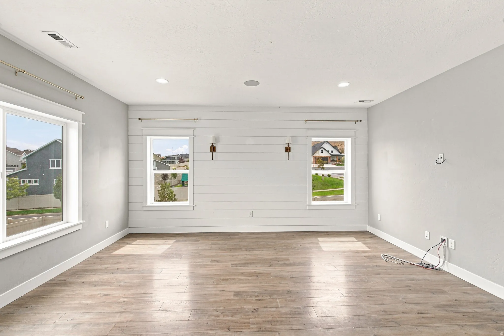 Wood-finish flooring, recessed lighting, and a shiplap accent wall with two sconces
