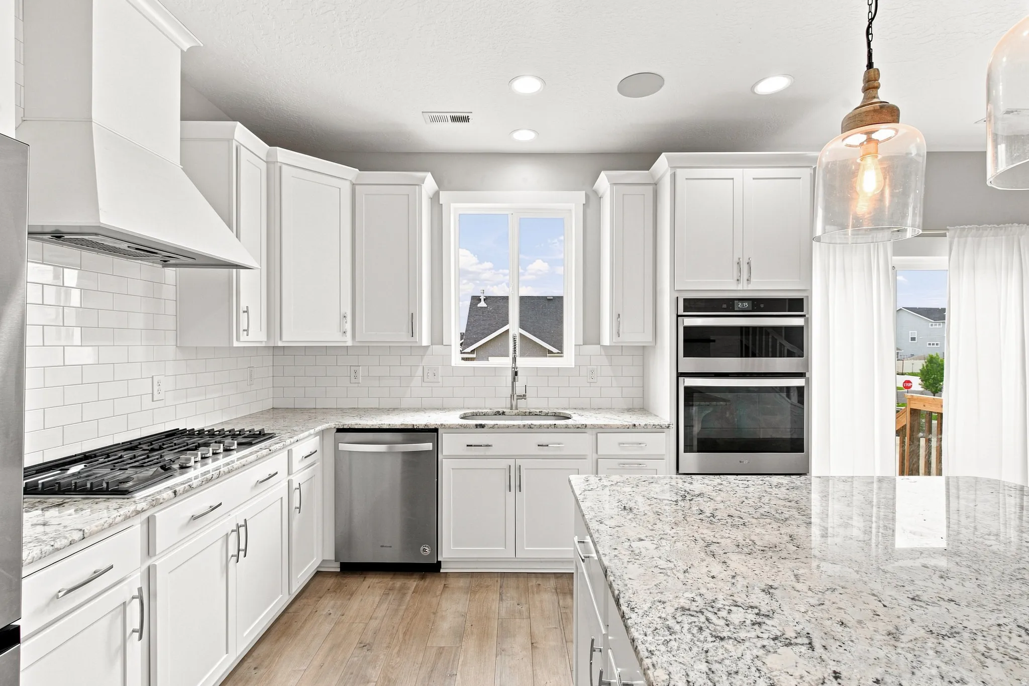 White shaker cabinetry, stainless steel appliances, wood-finish flooring, white subway tile backsplash, and light-toned countertops