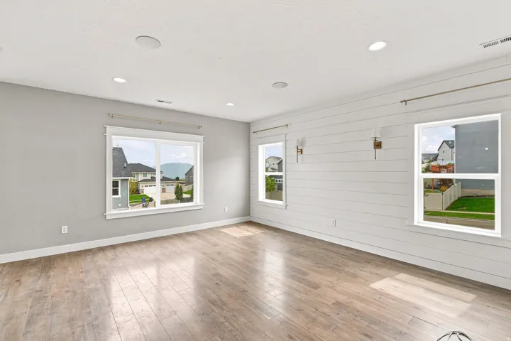 Wood-finish flooring with a shiplap accent wall, multiple windows, recessed lighting, and wall-mounted sconces