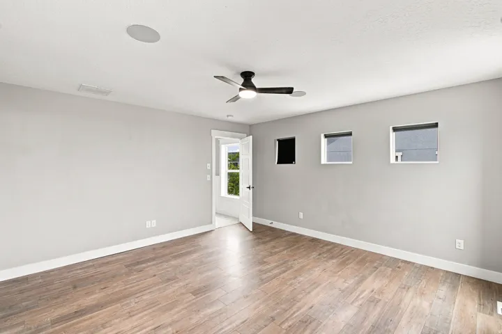 Recessed ceiling speaker, contemporary ceiling fan, three square windows, wood-finish flooring, white trim details