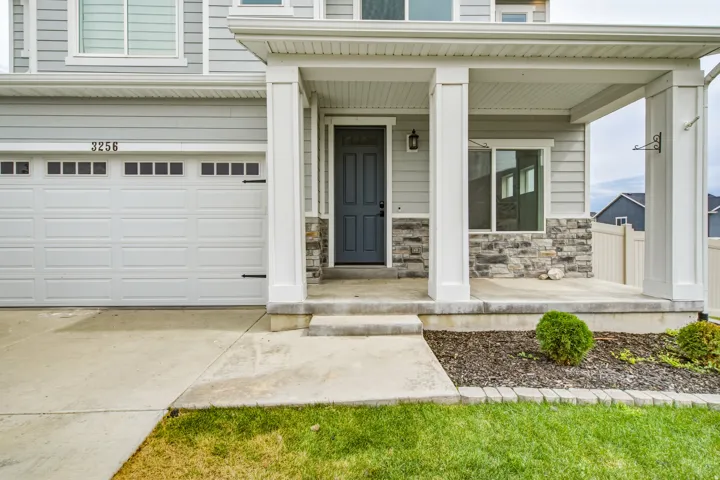 Covered front porch with stone accent pillars, light gray siding, and a paneled garage door