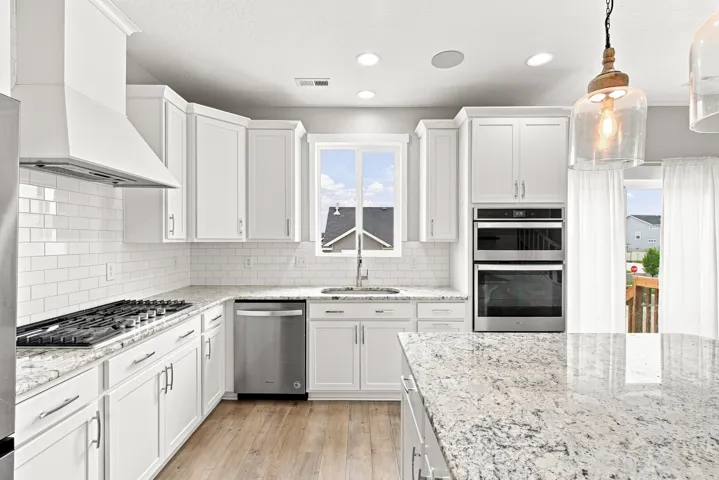 White shaker cabinetry, stainless steel appliances, wood-finish flooring, white subway tile backsplash, and light-toned countertops