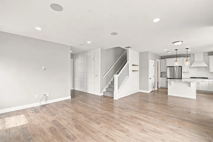 Wood-finish flooring, recessed ceiling lighting, kitchen island with pendant lighting, stainless steel refrigerator, and subway tile backsplash