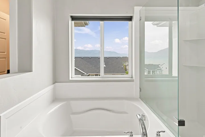 Built-in soaking tub with chrome fixtures, framed window with mountain and water backdrop, and a glass-enclosed shower