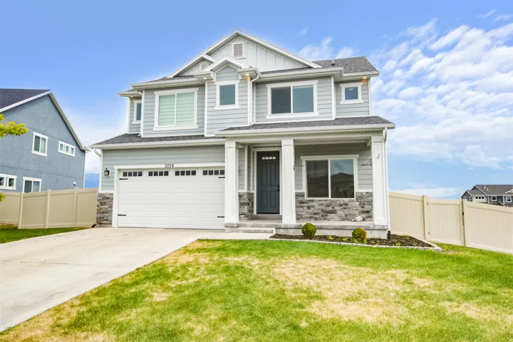 Two-story residence featuring light gray siding with white trim, stone veneer accents, an attached two-car garage, covered entry, and a light-colored privacy fence