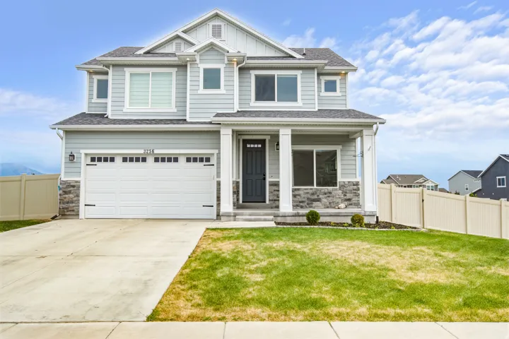 Two-story residence featuring light gray siding with stone accents, a covered front porch, and a two-car garage