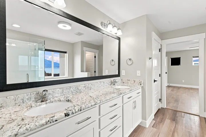 Dual vanity with undermount sinks, stone countertops, white shaker cabinetry, and wood-finish flooring