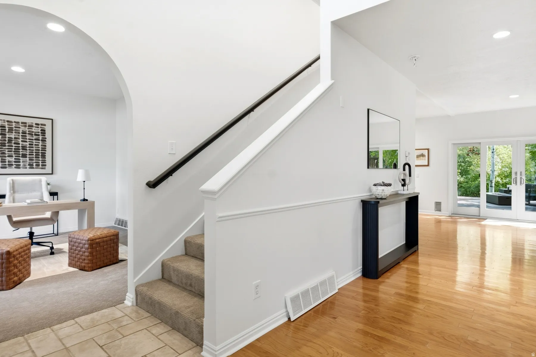 Carpeted staircase with black handrail, arched doorway, and recessed lighting