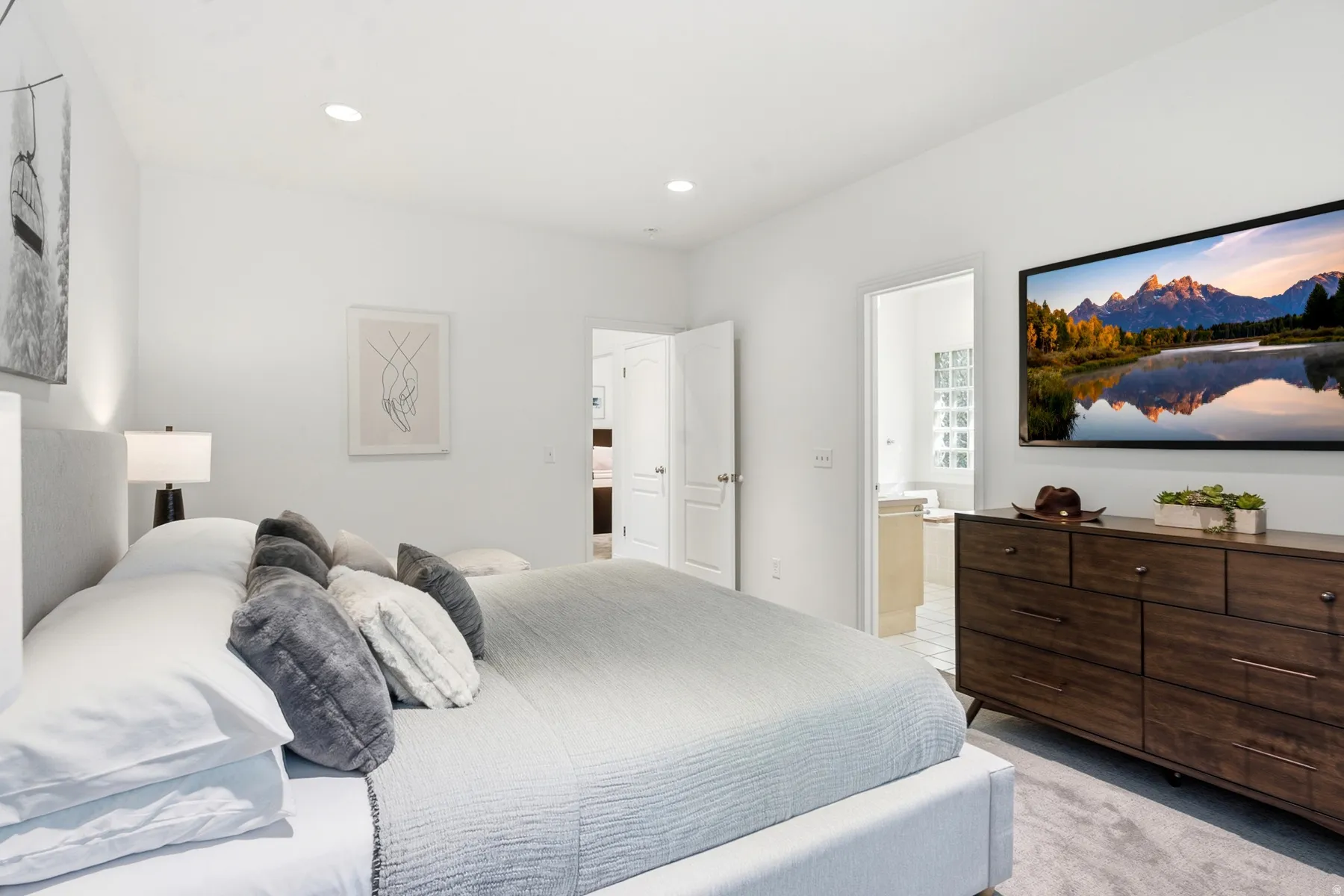 Recessed lighting, light gray carpeting, and a light-toned fabric bed frame