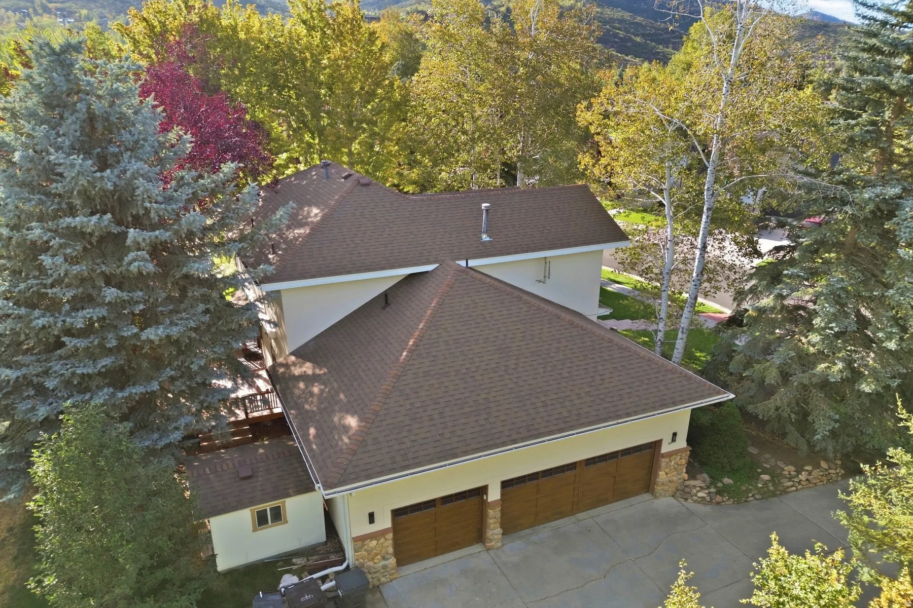 Multi-level dwelling featuring a two-car garage with wood-finish doors, stone accents, and a shingle roof