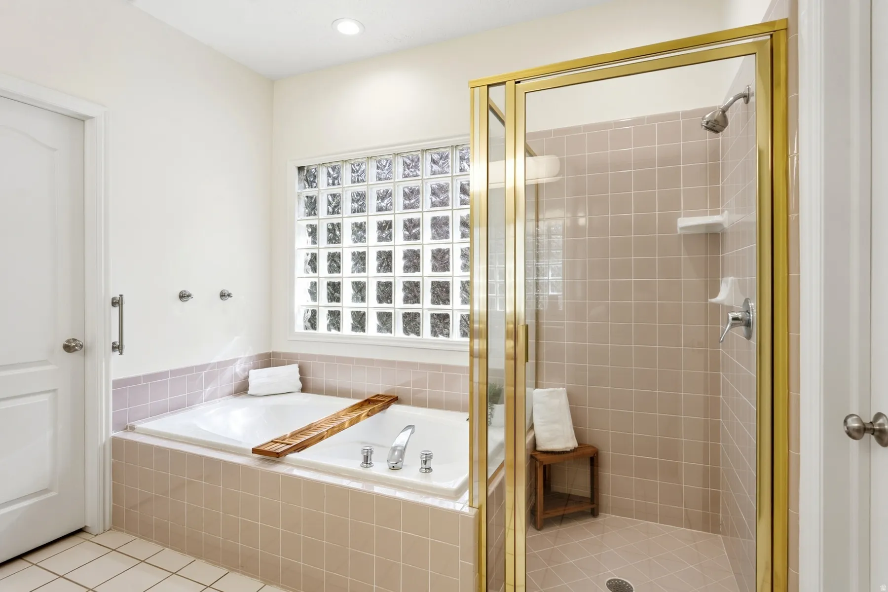 Recessed lighting, glass block window, built-in soaking tub, tile flooring, and a glass-enclosed shower with a gold-tone frame