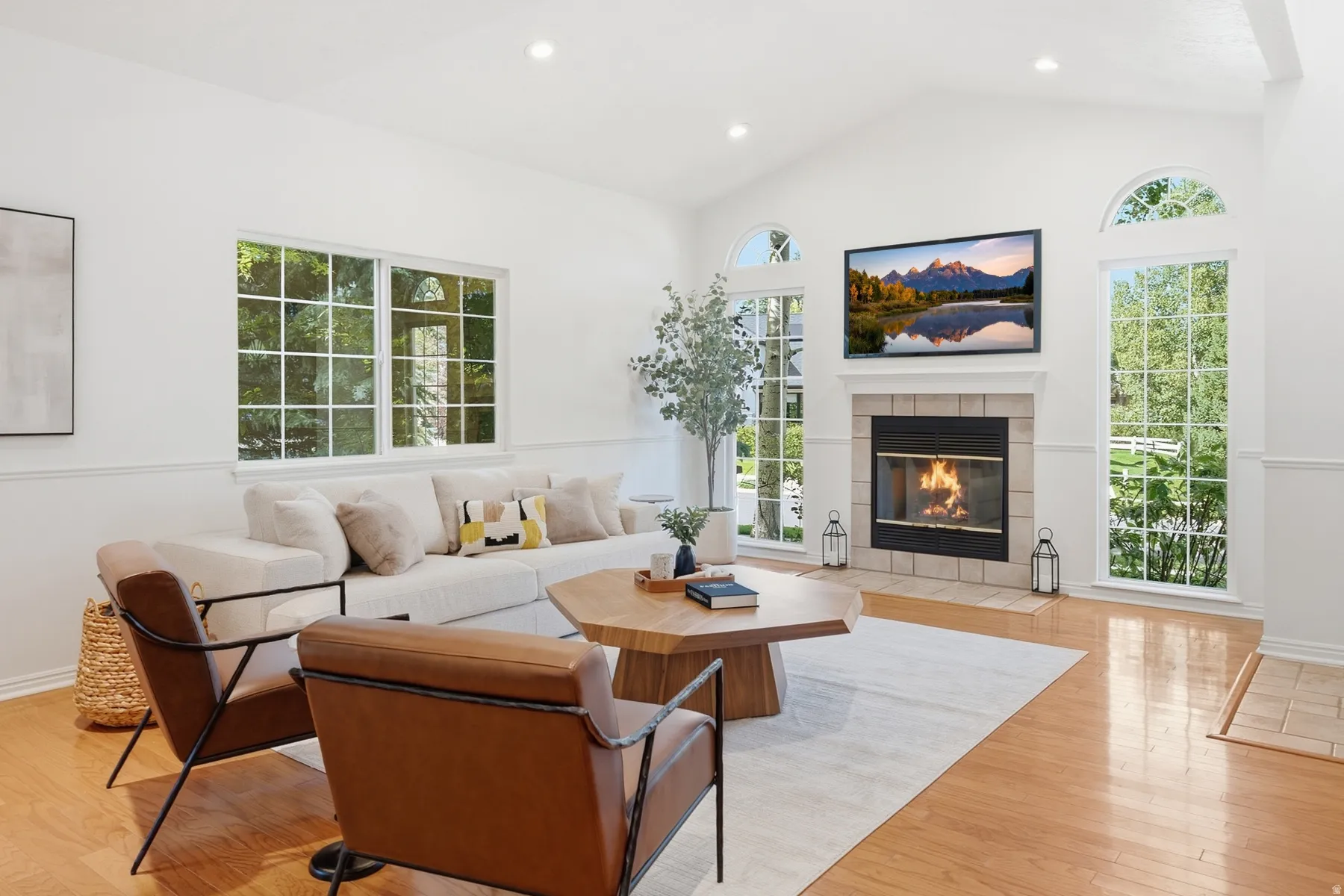 Vaulted ceiling, stone surround fireplace, arched windows, light wood-finish flooring, and recessed lighting