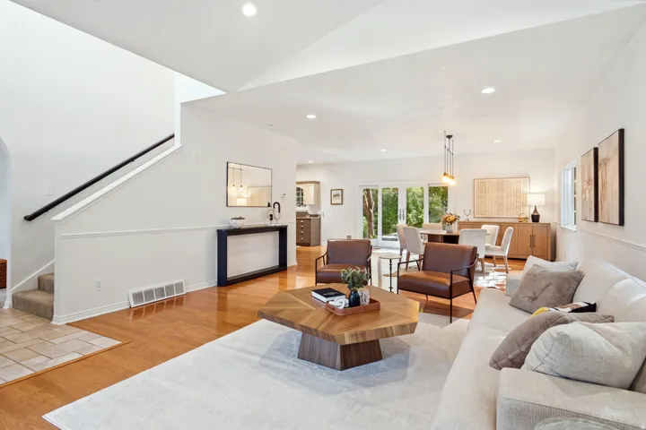 Recessed lighting, wood flooring, white walls, and a staircase with a black handrail