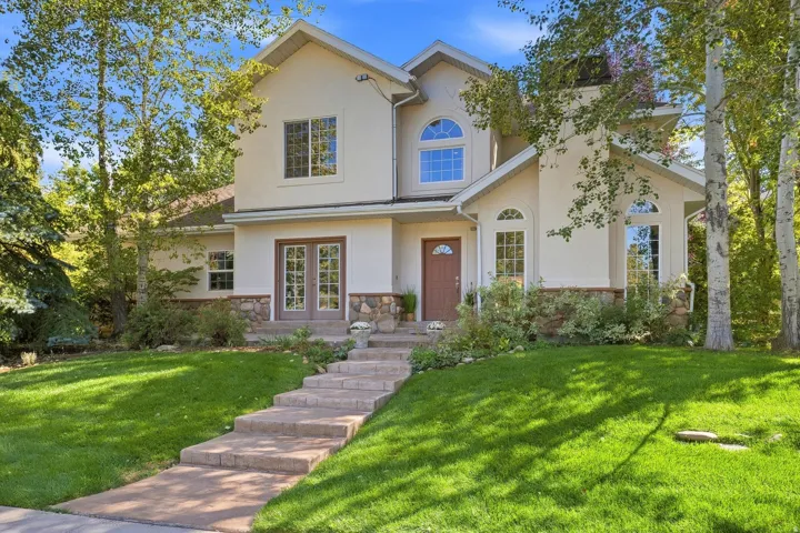 Stucco exterior with stone accents, arched windows, transom windows, double French doors, and mature trees