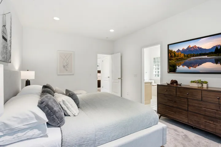 Recessed lighting, light gray carpeting, and a light-toned fabric bed frame