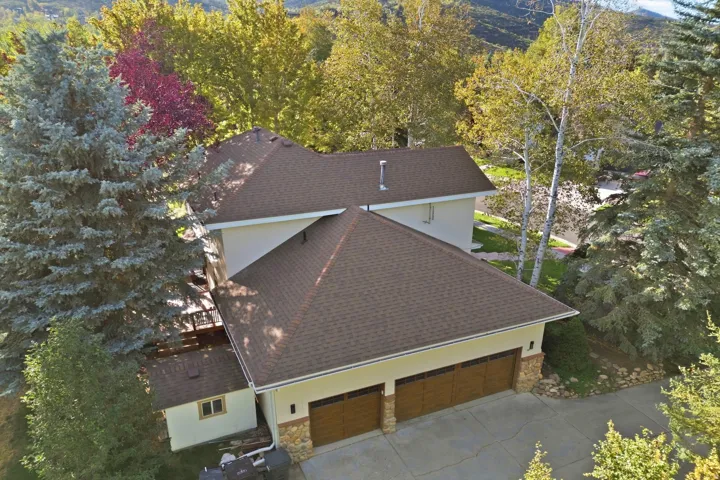 Multi-level dwelling featuring a two-car garage with wood-finish doors, stone accents, and a shingle roof