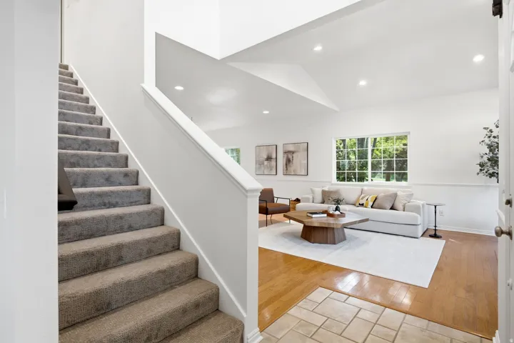 Carpeted staircase with white balustrade, wood-finish flooring, tiled entry, and vaulted ceilings with recessed lighting