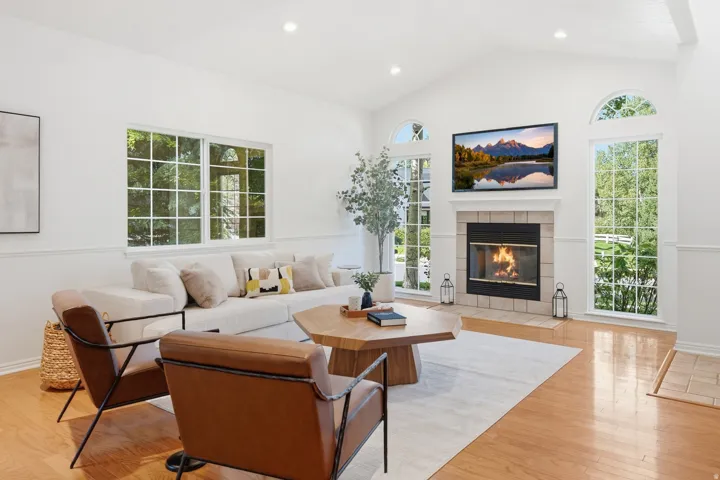 Vaulted ceiling, stone surround fireplace, arched windows, light wood-finish flooring, and recessed lighting