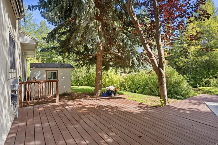 Expansive wood-finish decking, mature trees, a detached storage shed, and a raised wooden railing